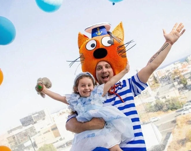 Children’s party entertainer in a sailor costume holding a girl with balloons around