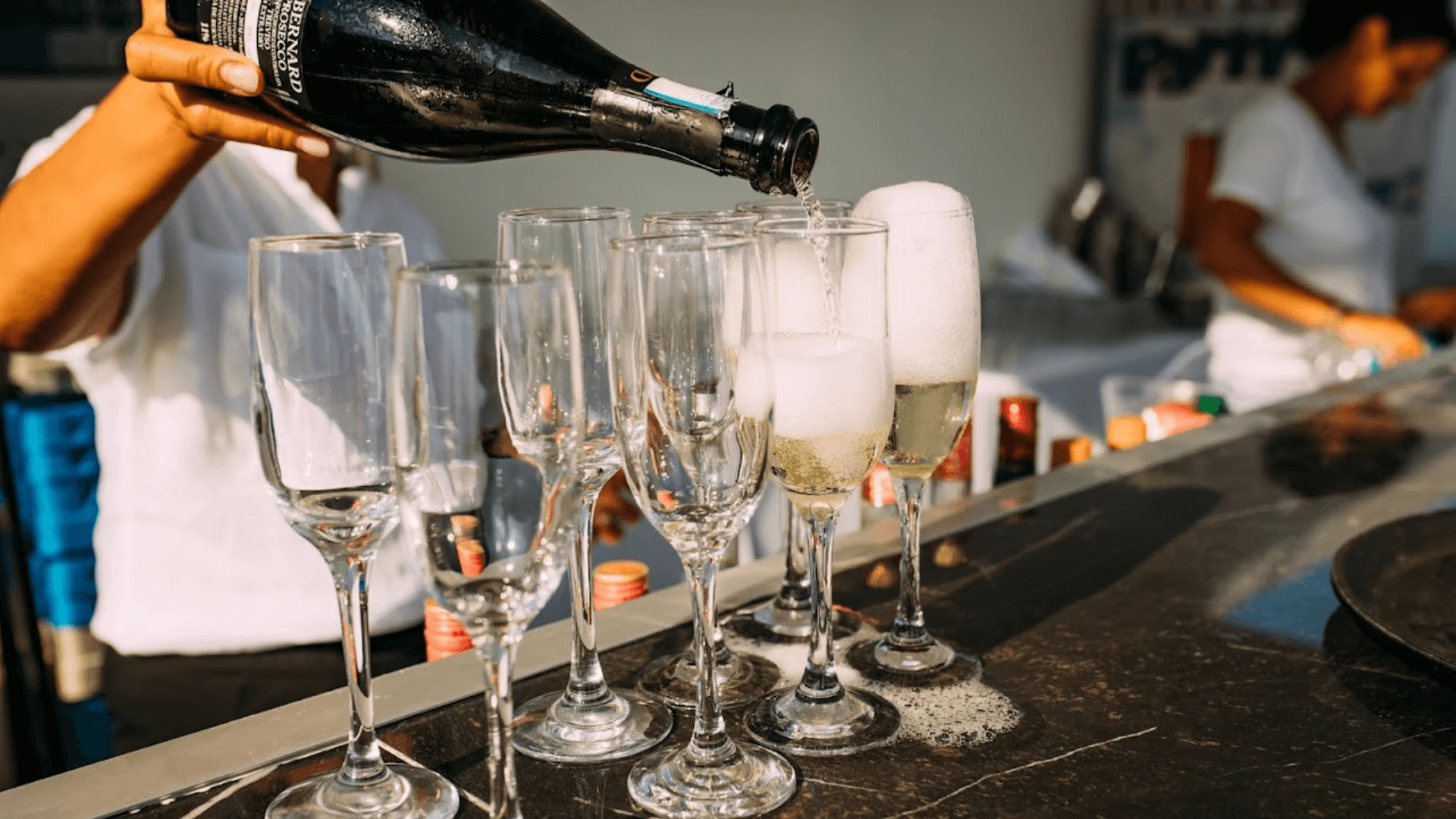 Bartender pouring prosecco into rows of glasses at a party in Limassol