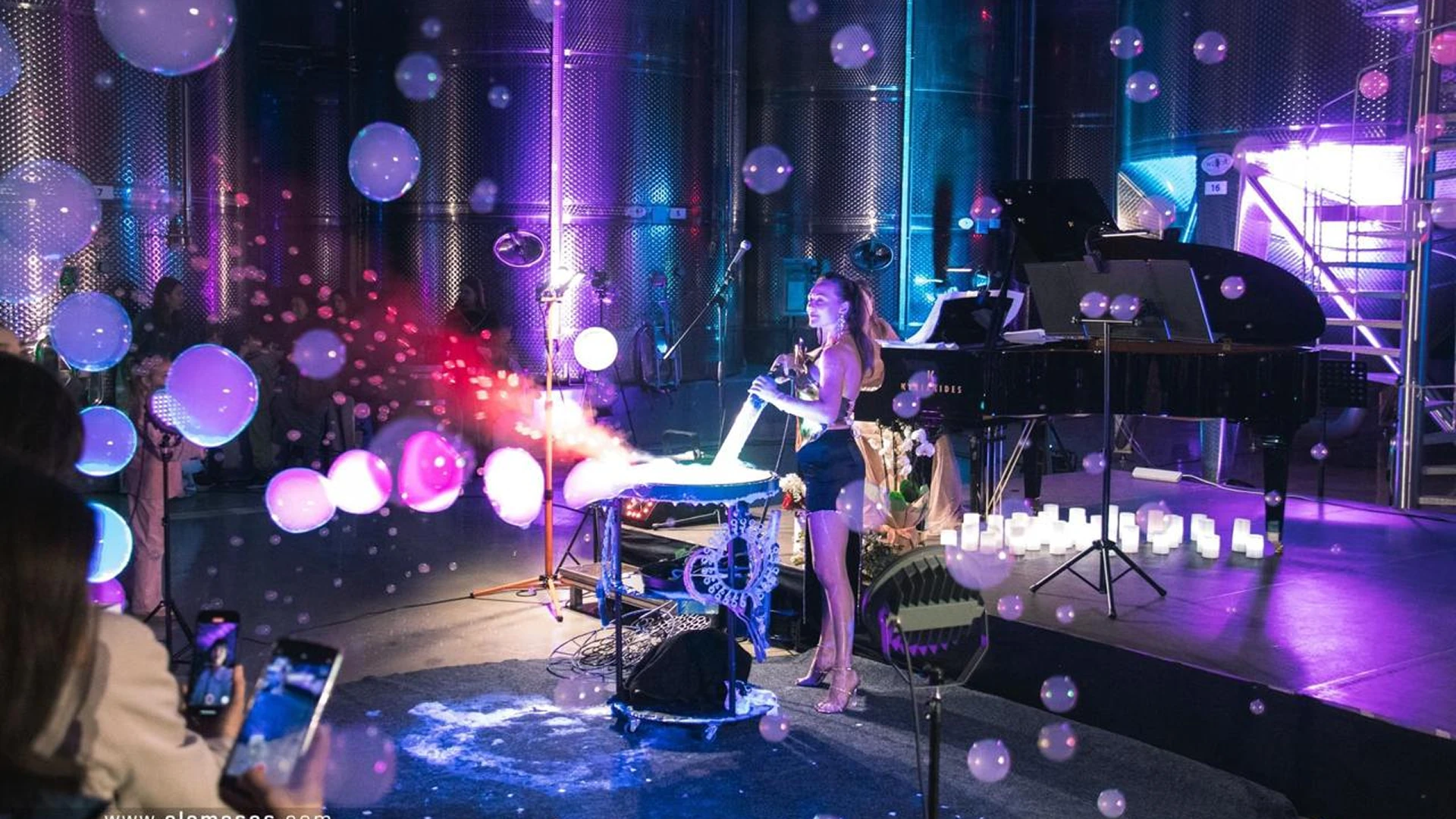 A female performer creating large smoke-filled bubbles on a stage with purple lighting and a grand piano during a corporate event.