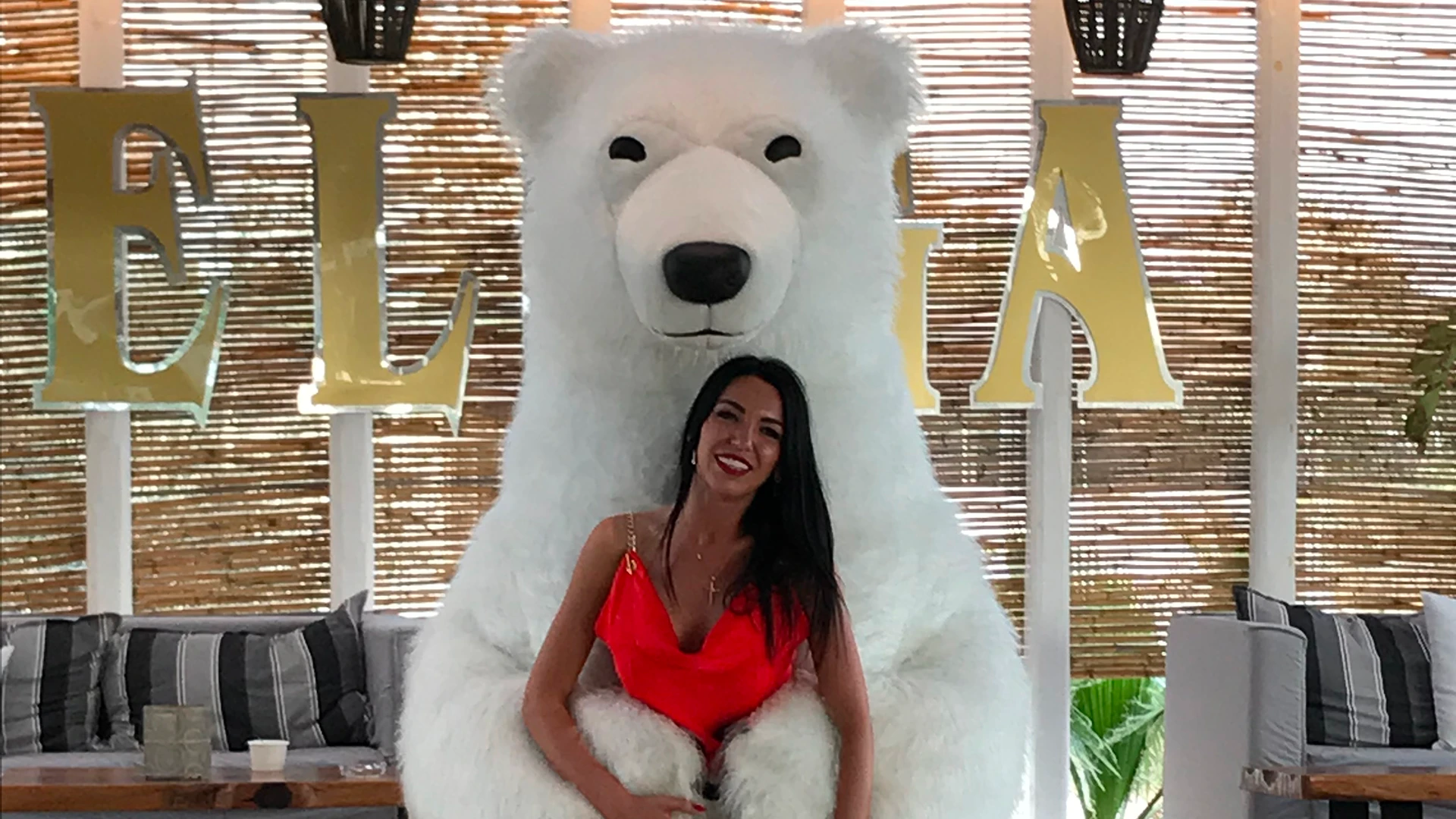 A smiling woman in a red dress posing for a photo with a giant Great White Bear mascot at a corporate event venue.