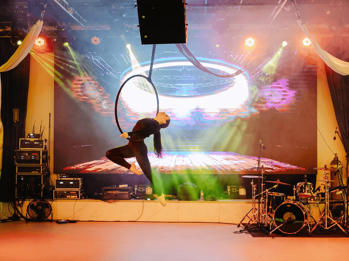 Aerial performer posing on a suspended hoop in front of an LED screen with stage lighting