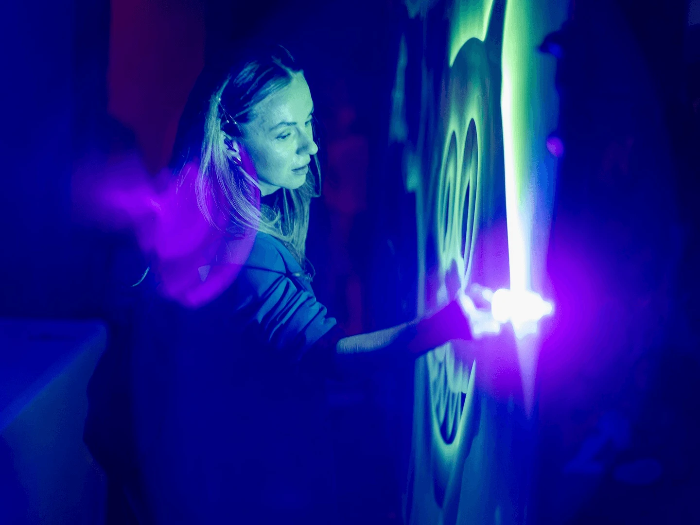 Performer creating a glowing light drawing on a dark stage lit in blue and violet