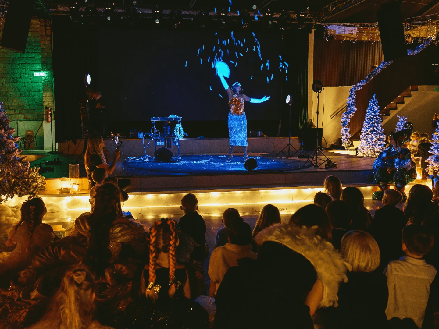 Bubble show performer under ultraviolet lighting on stage with an audience watching from below