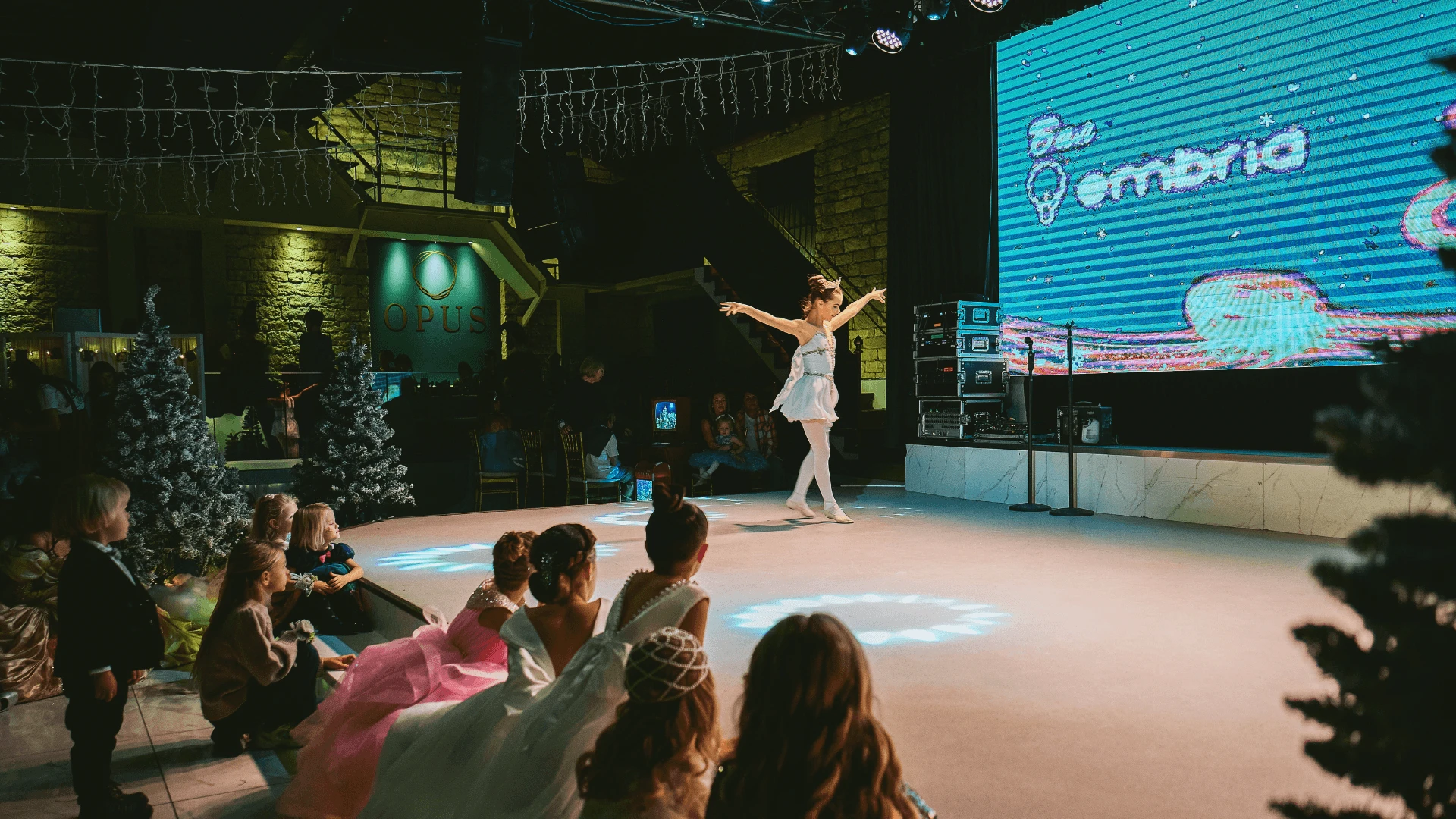 Performer creating glowing blue bubbles in a darkened hall during a neon bubble show