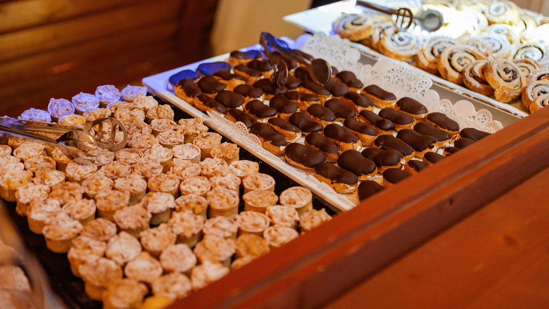 Dessert buffet with eclairs, tartlets and pastries laid out on wooden serving counters