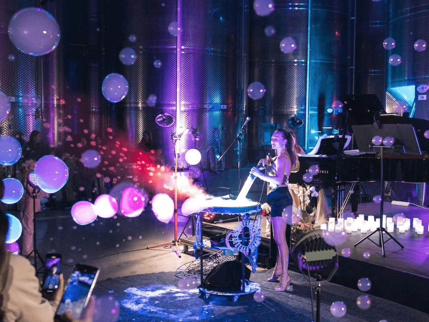 Bubble show performer beside a grand piano in a winery hall, guests filming on phones