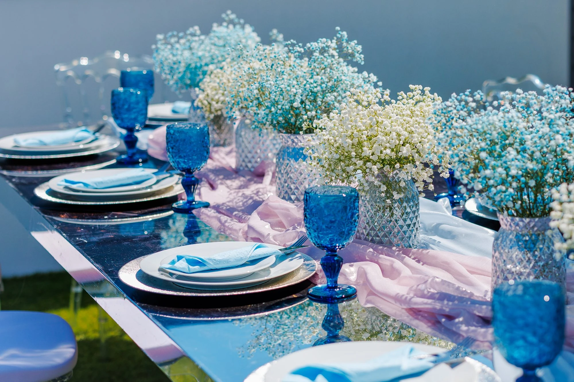 Table setting: blue glassware, baby's breath and a mirrored tabletop on a terrace