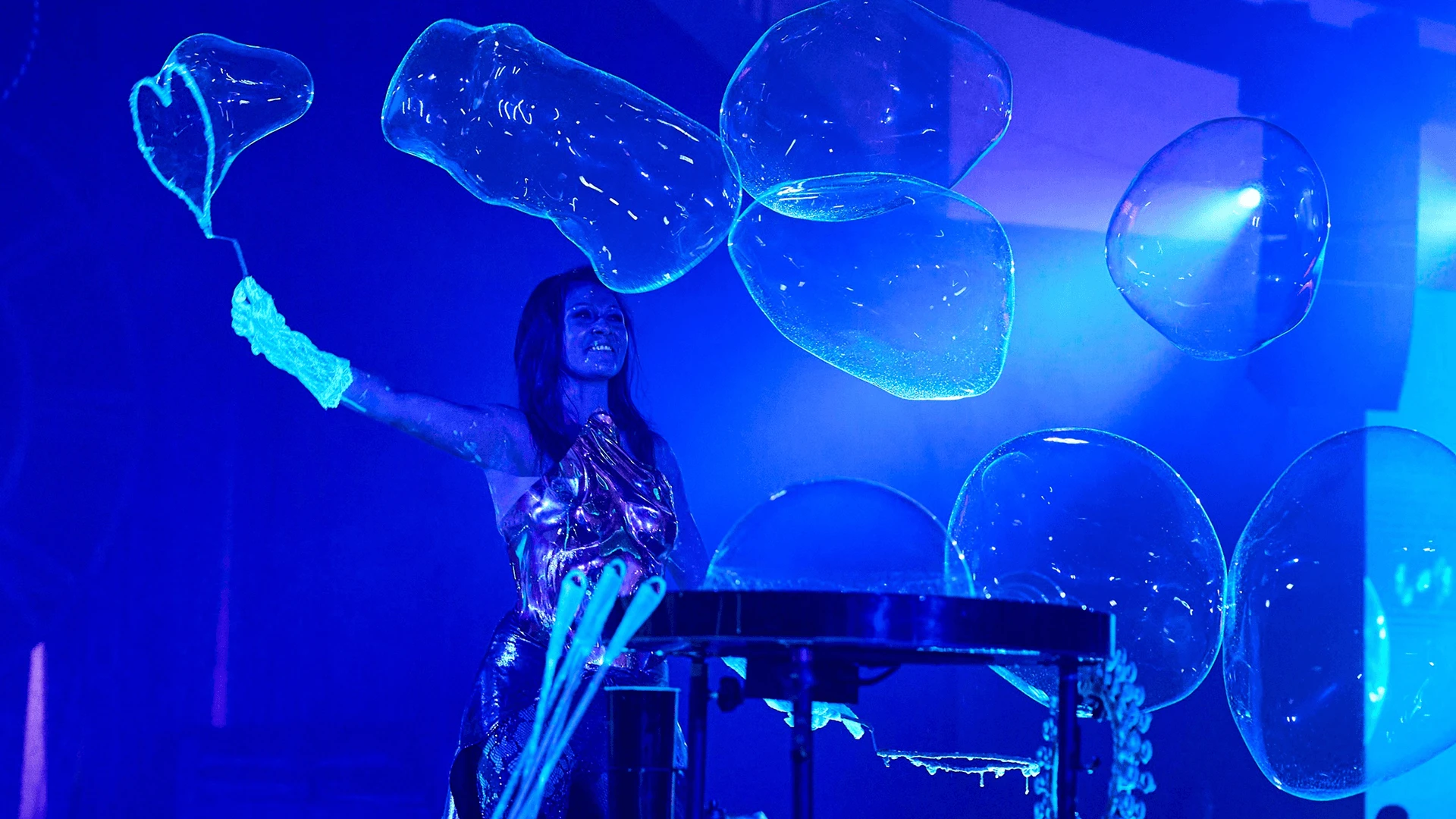 Performer creating large bubbles under blue stage lighting during a corporate show programme